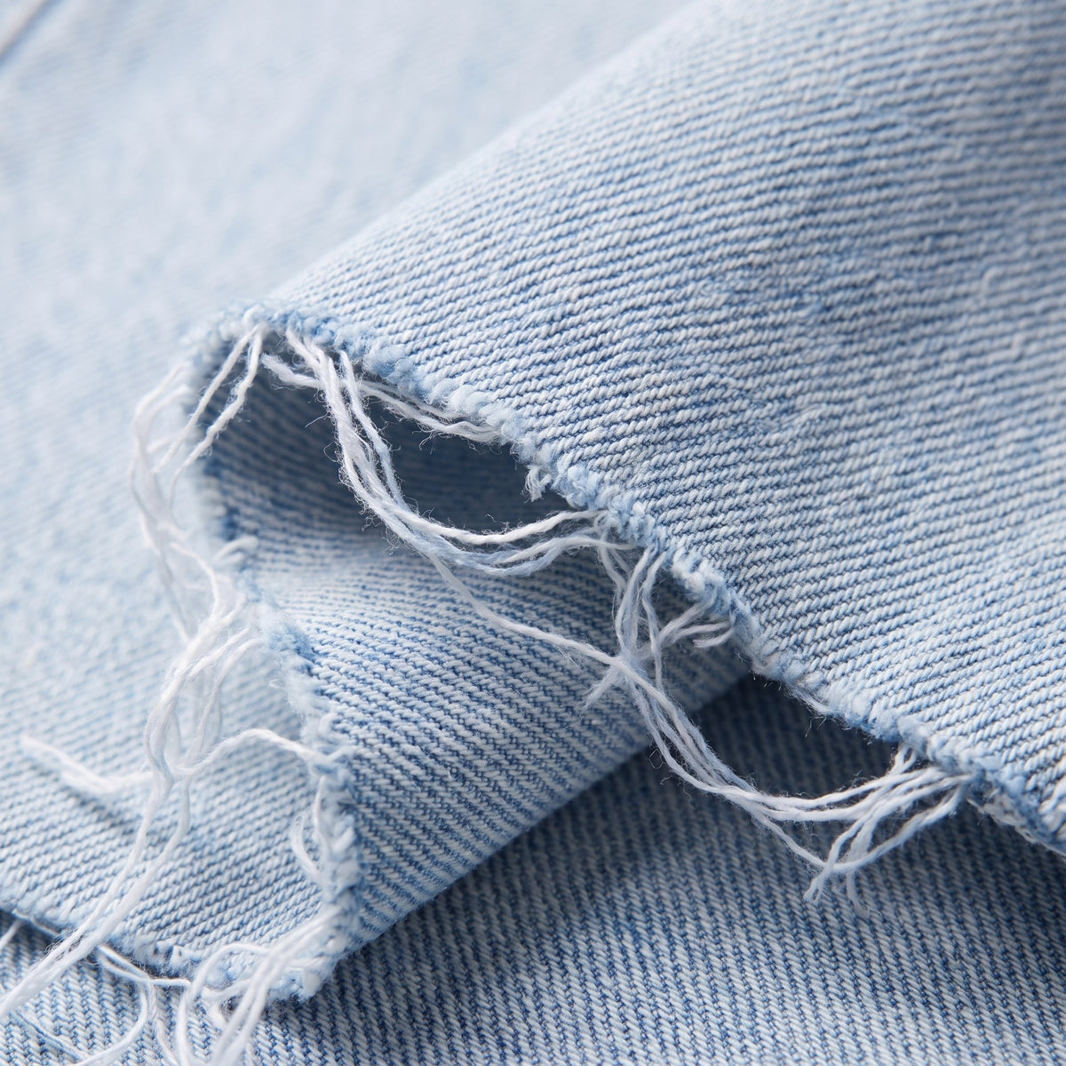 Savona distressed jeans fabric detail, light wash denim and raw frayed hem close-up