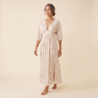 Beige tropical print maxi dress, walking pose on model, warm cream studio background