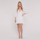 White cotton-linen tiered mini dress with crochet-lace V-neck and 3/4 puff sleeves, full-length front view