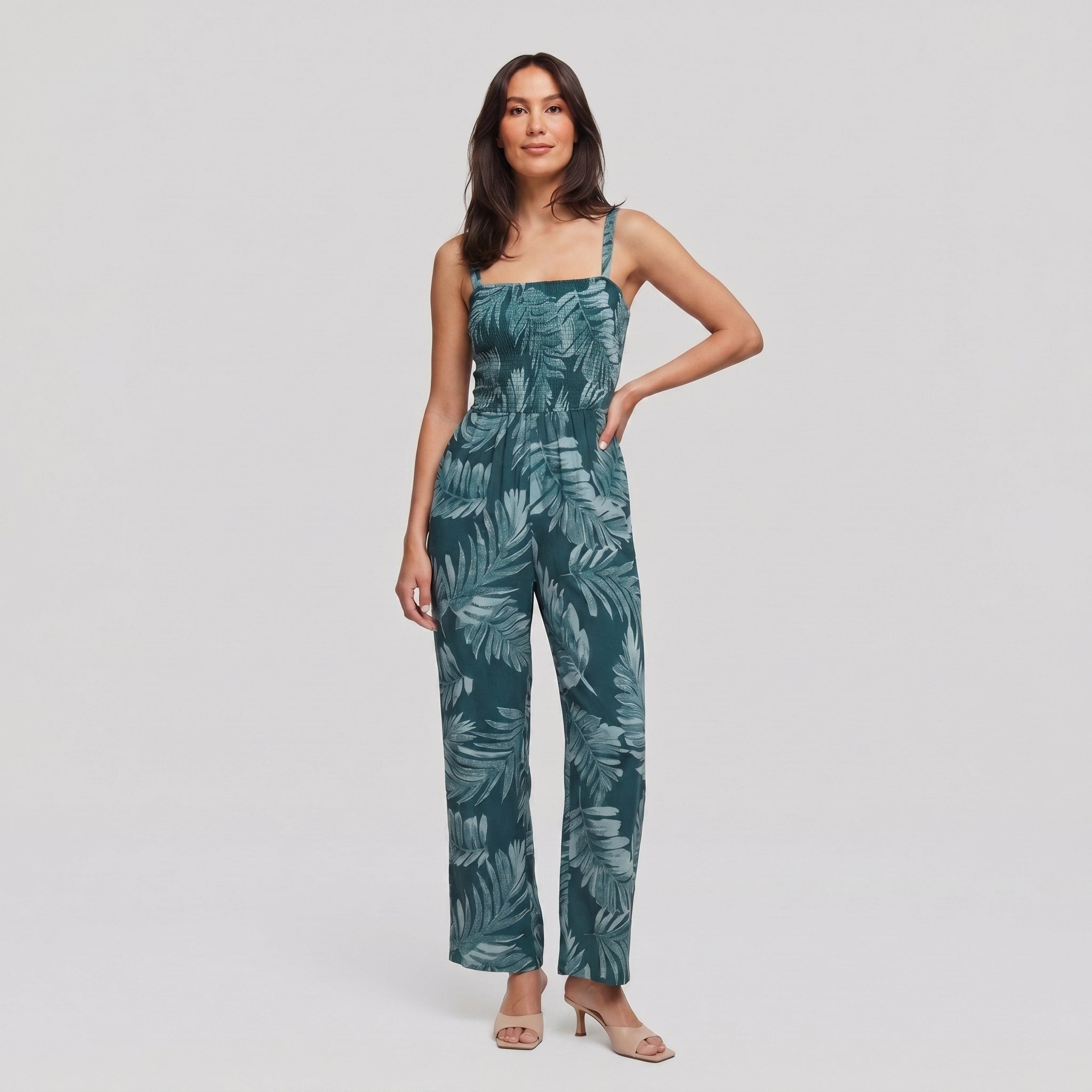Model wearing teal wide-leg jumpsuit with smocked bodice, hand on hip